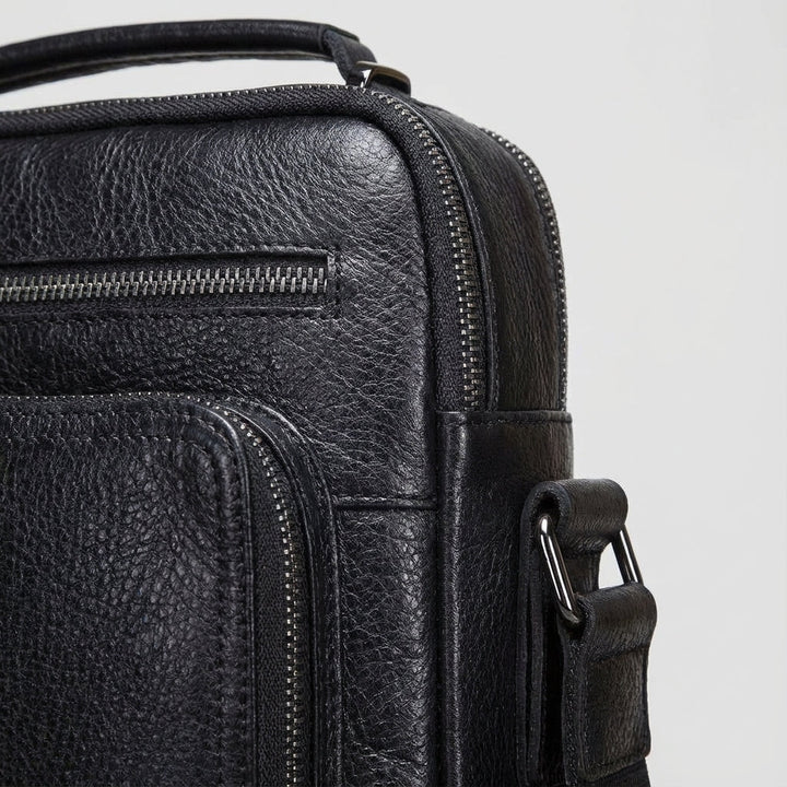 Heren draagt compacte zwarte leren messenger tas comfortabel over de schouder voor een moderne, stijlvolle look.