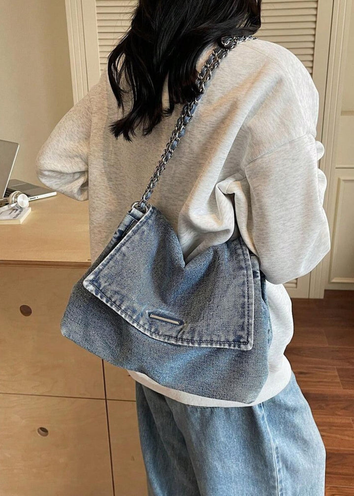 Dames schoudertas van denim met chique metallic ketting, gedragen over de schouder.