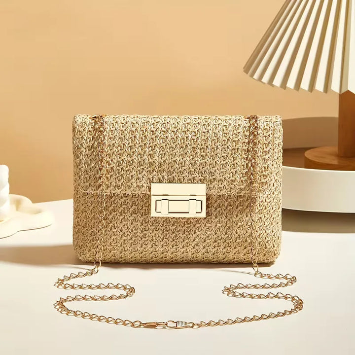 Compacte dames schoudertas van stro met gouden accenten, geschikt als handtas voor de zomer.