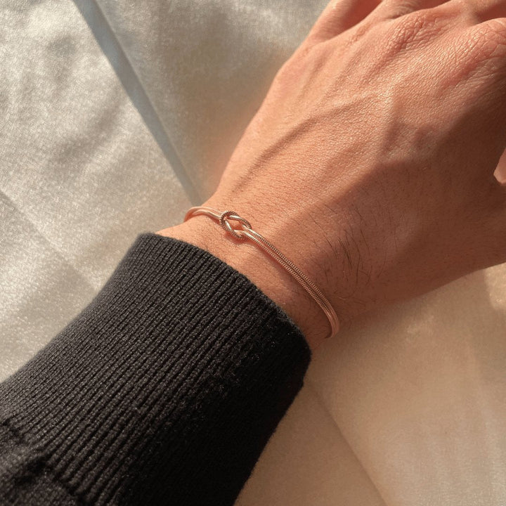 Gedetailleerde foto van damesarmband met liefdesknoop, goudkleur.