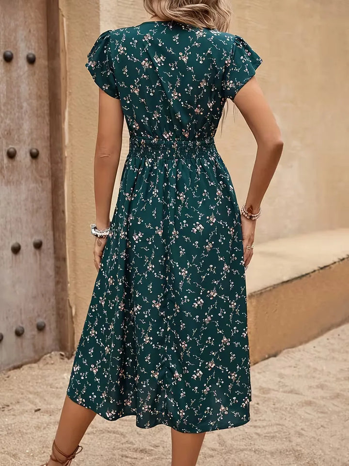 Comfortabele A-lijn zomerjurk met vrolijke bloemenprint, V-hals en luchtige fluttermouwen. Gesmokte taille, petrol.