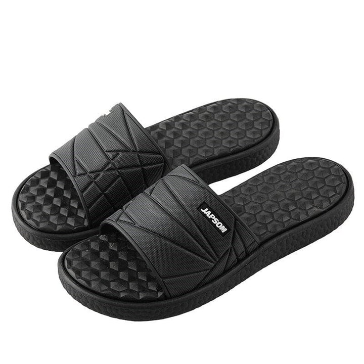 Paar orthopedische herenslippers in beige, op een stenen pad, klaar voor een wandeling.