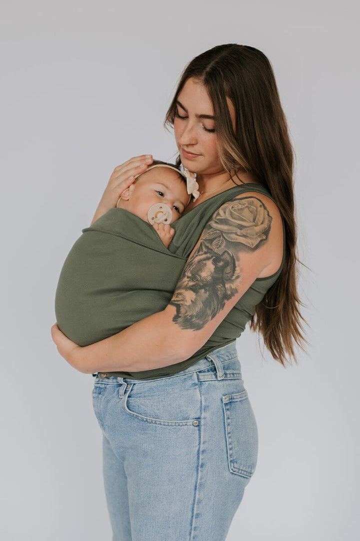 Glimlachende ouder en baby dicht tegen elkaar in zacht draagshirt; bevordert bonding, veiligheid en geborgenheid.