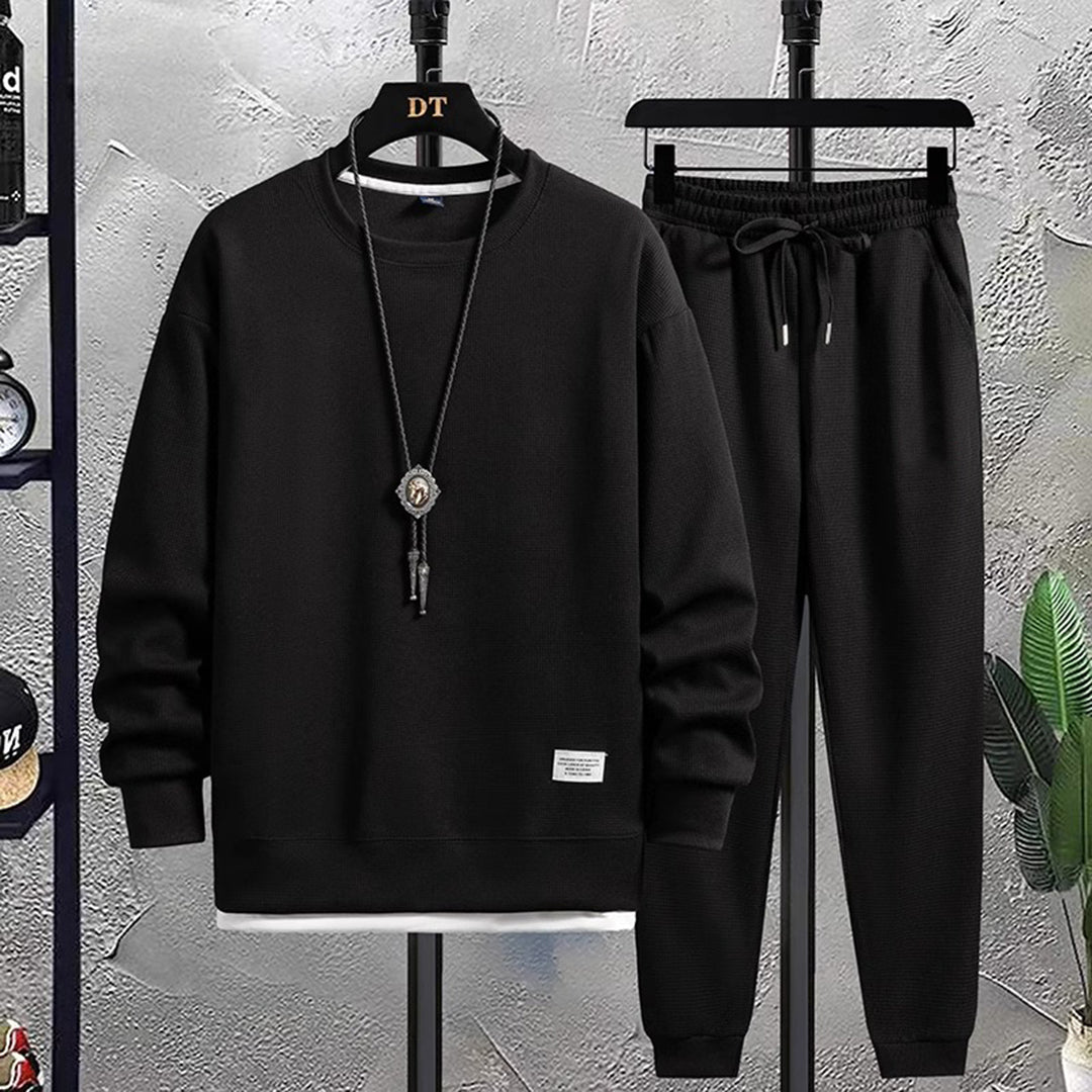 Model draagt het complete zwarte heren joggingpak, toont de casual en comfortabele stijl.
