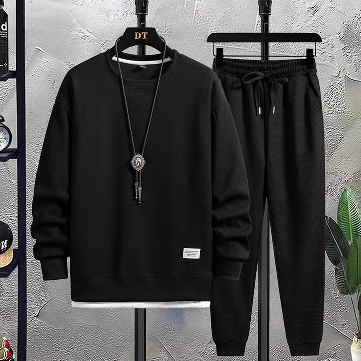Model draagt het complete zwarte heren joggingpak, toont de casual en comfortabele stijl.