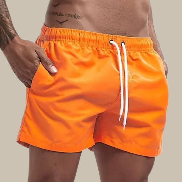 Model in een rode sneldrogende zwembroek, toont de pasvorm en de bewegingsvrijheid van deze herenmode item.