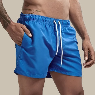 Man lachend in sneldrogende zwembroek aan het strand, casual zomerkleding, geschikt voor wateractiviteiten.